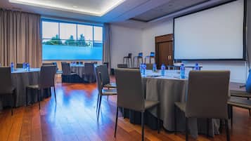 Un salón de conferencias con mesas, sillas y una pantalla para proyector.