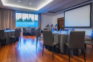 Un salón de conferencias con mesas, sillas y una pantalla para proyector.