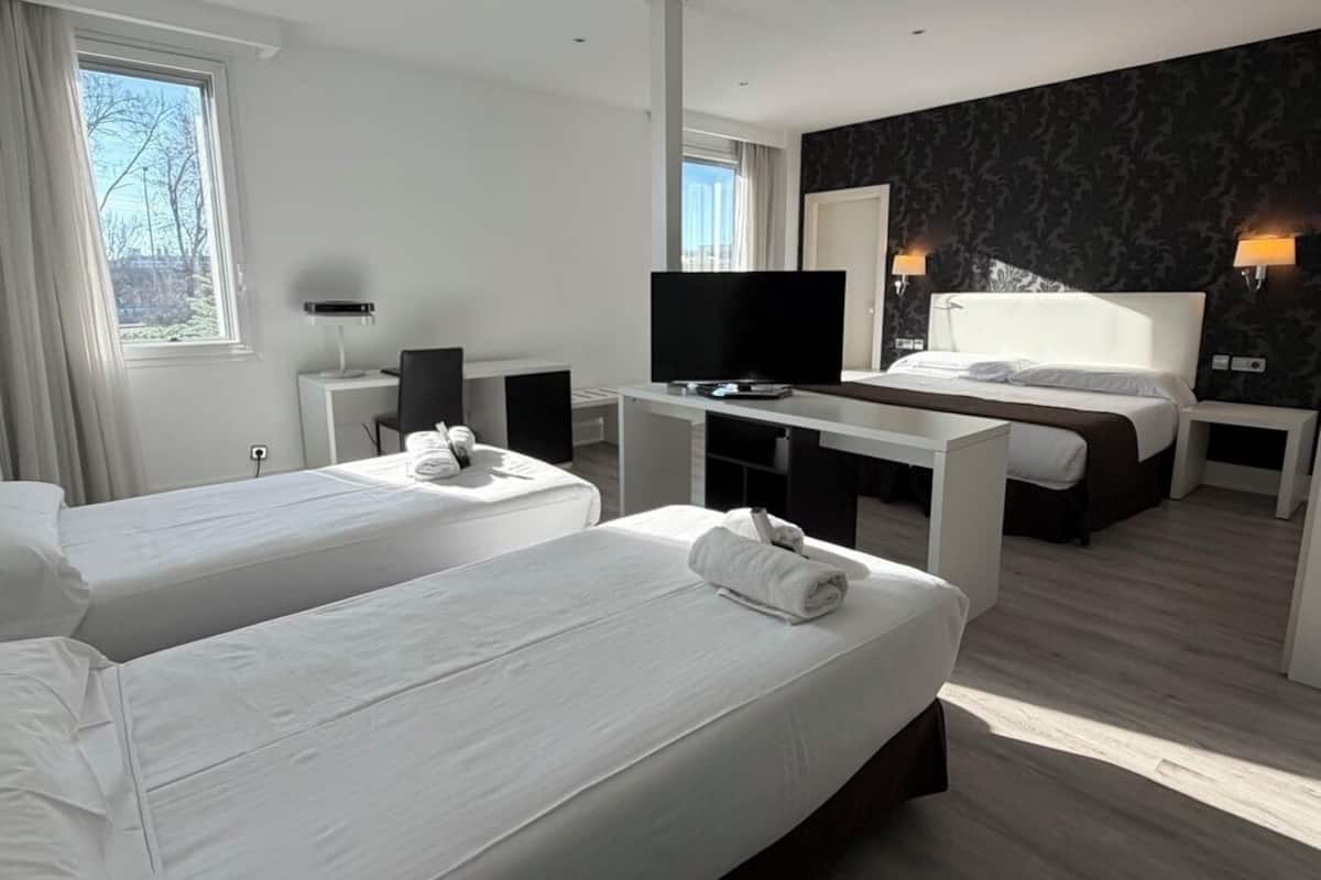 Une chambre d’hôtel avec deux lits, un bureau avec une télévision et un mur à motifs sombres.