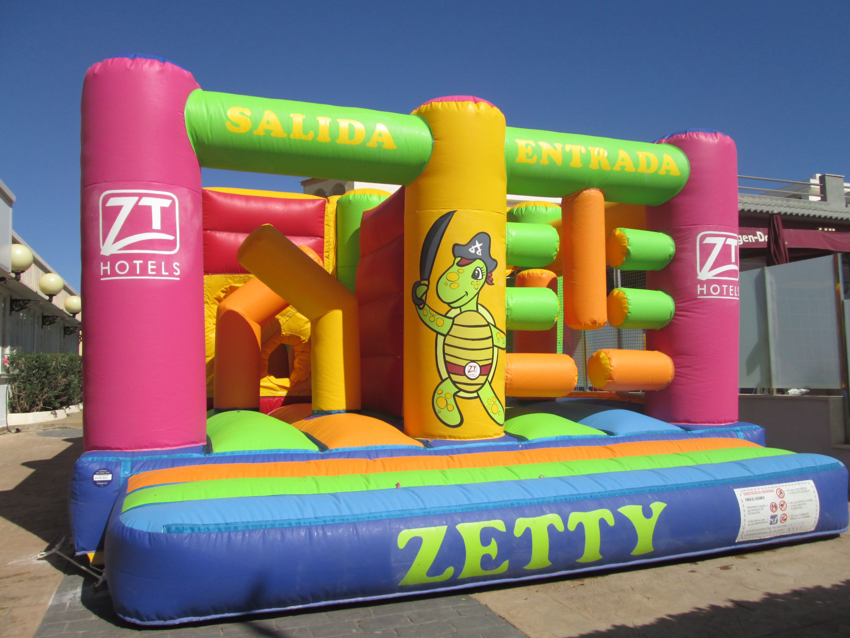 An inflatable bouncy castle with "SALIDA" and "ENTRADA" signs, a turtle character, and the "ZETTY" logo.