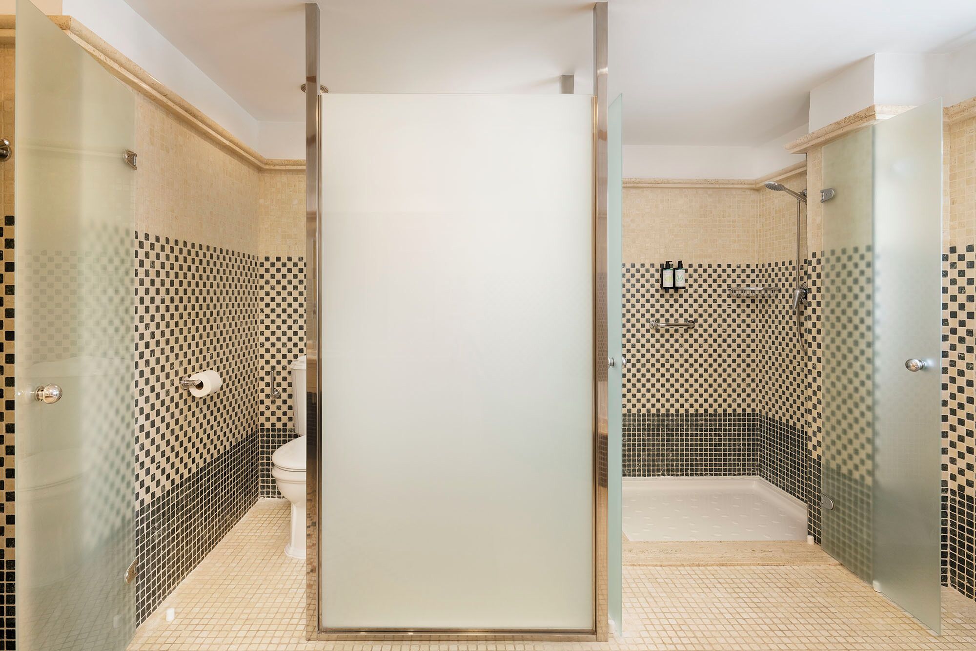 Un baño con mampara de vidrio, inodoro, zona de ducha y paredes con azulejos.