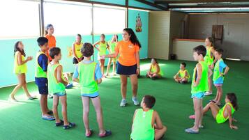 Un grupo de niños en una habitación con suelo verde y un ventanal grande, vistiendo chalecos llamativos.