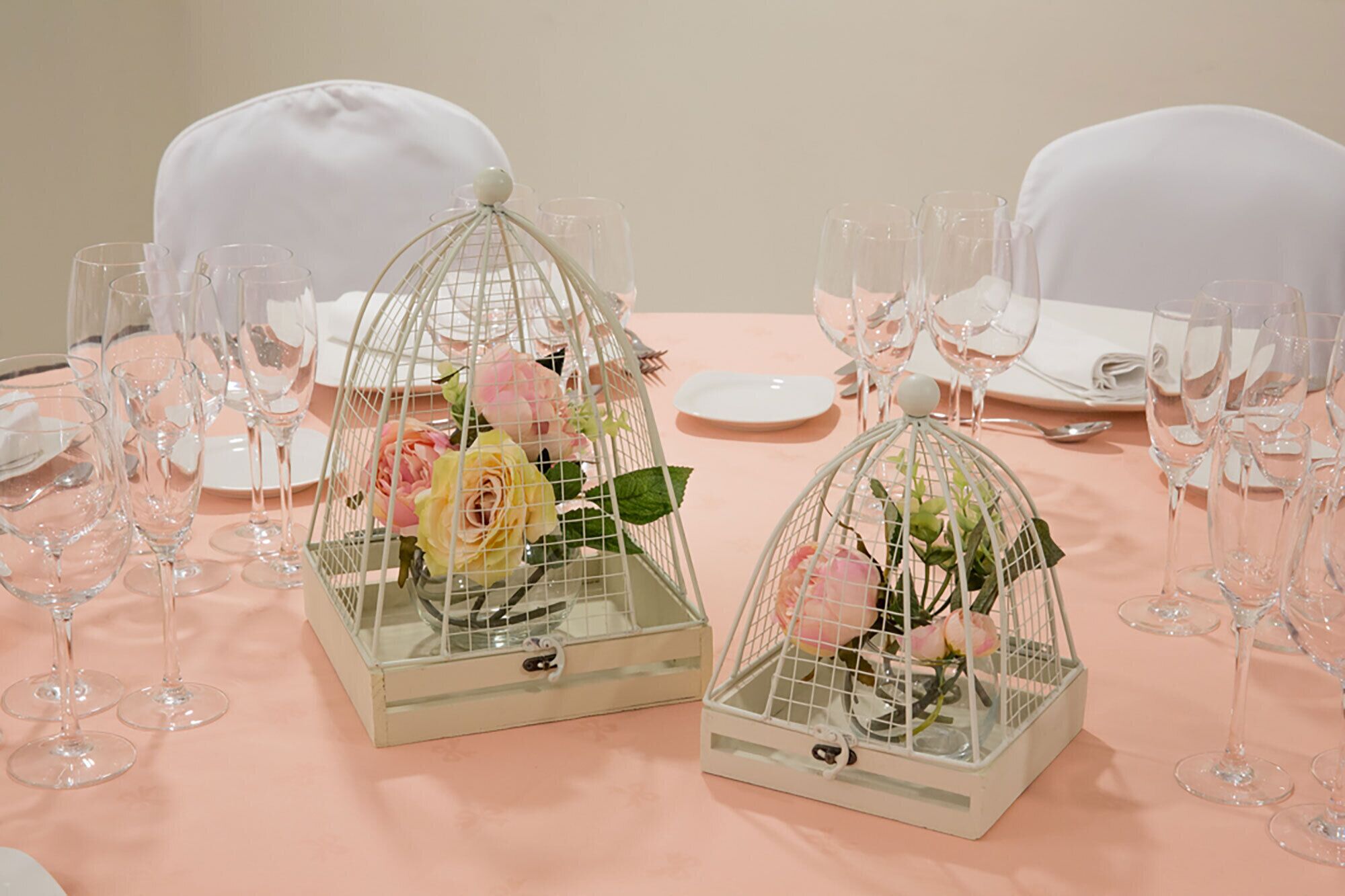 Una mesa dispuesta con copas de vino, platos y dos centros de mesa con jaulas y flores.