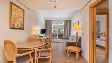 A hotel room with a dining area, a sofa, a TV, and a balcony with curtains.