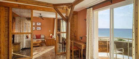 A room with a wooden ceiling, a balcony with a view of the sea, and a seating area with a table and chairs.