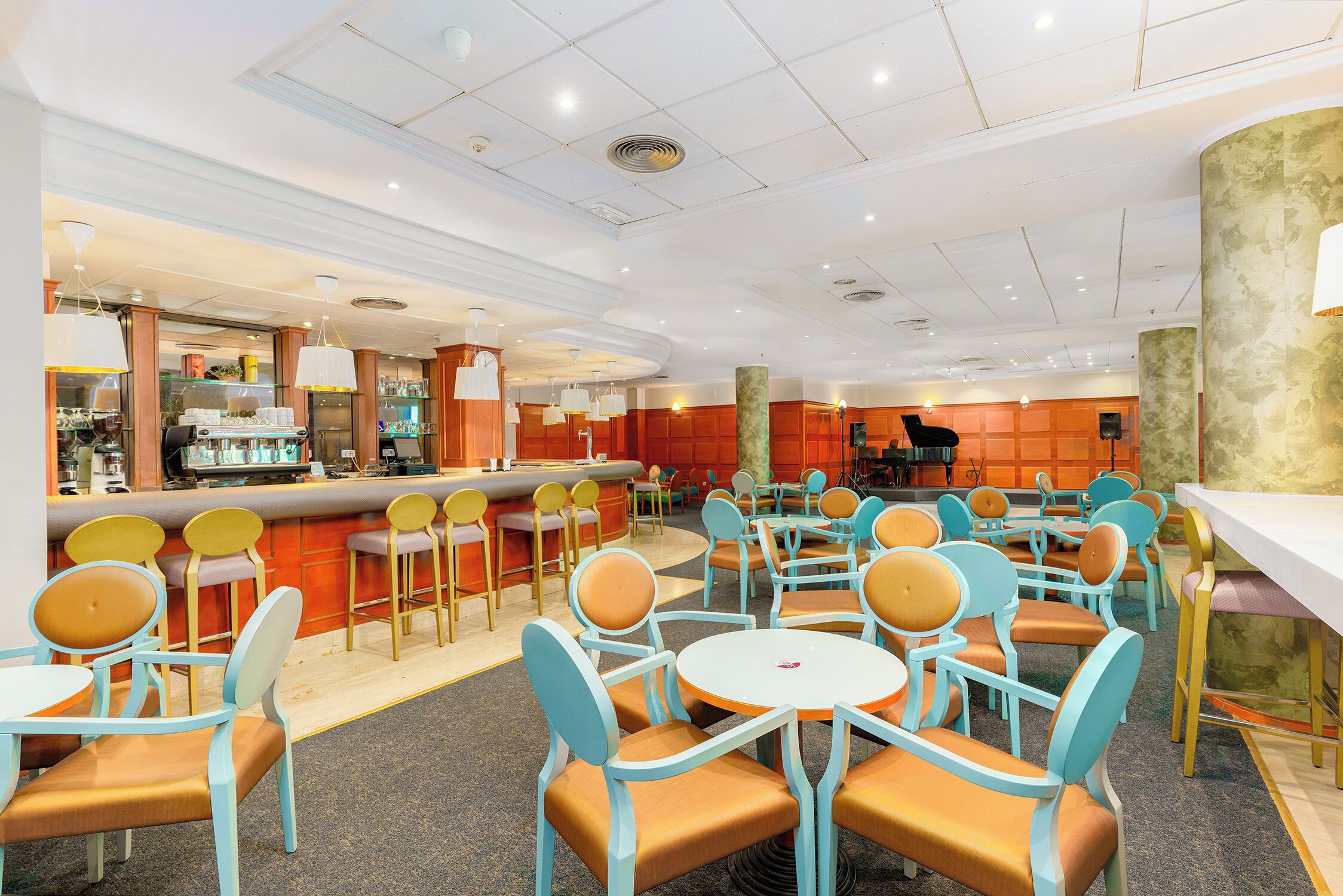 Un restaurante con mesas y sillas redondas, una zona de bar y un mostrador con productos a la vista.