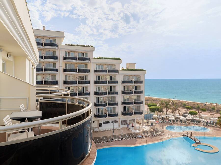 A hotel with multiple balconies overlooking a pool and beach.
