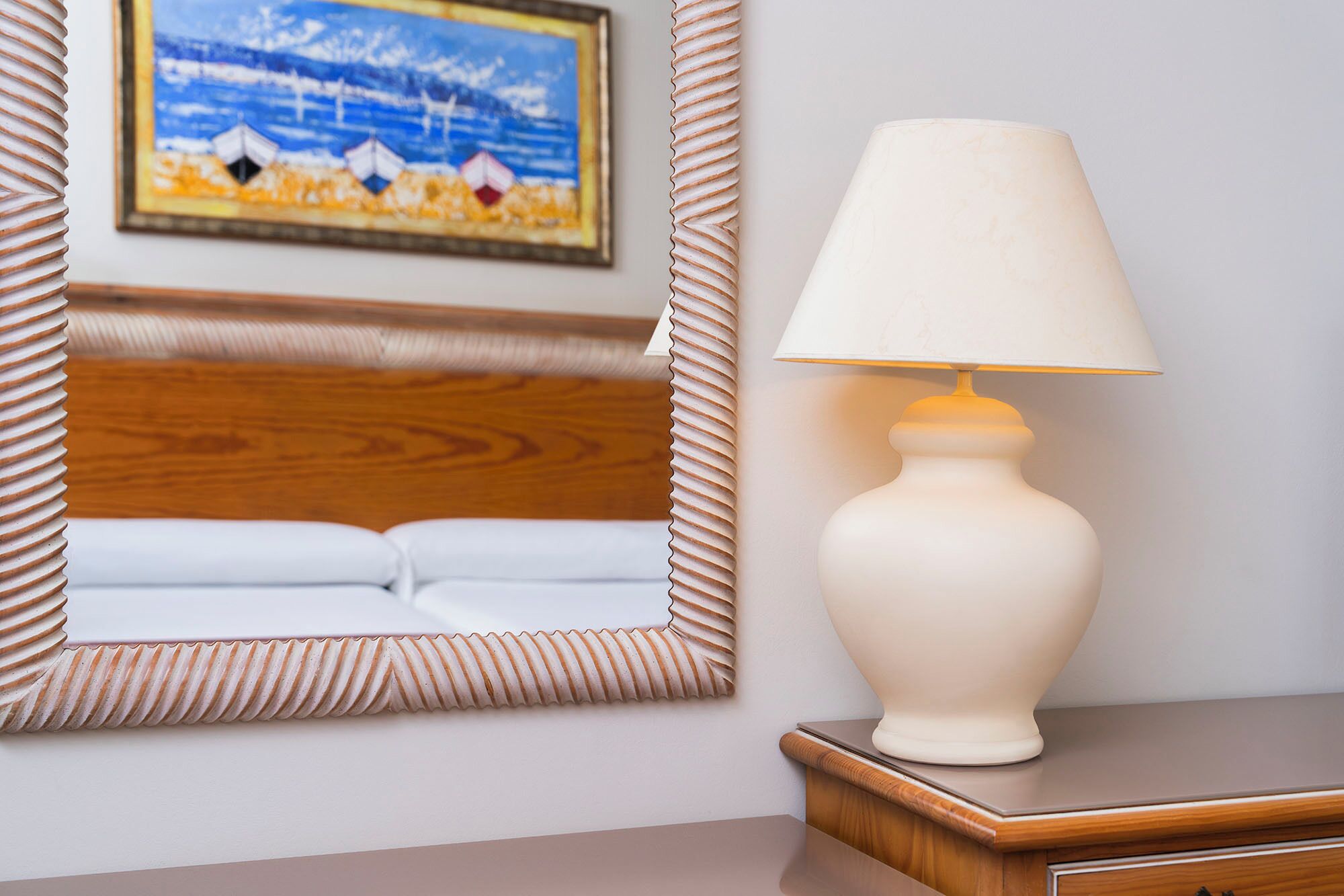 A hotel room with a wooden headboard, a bedside lamp, and a framed painting on the wall.