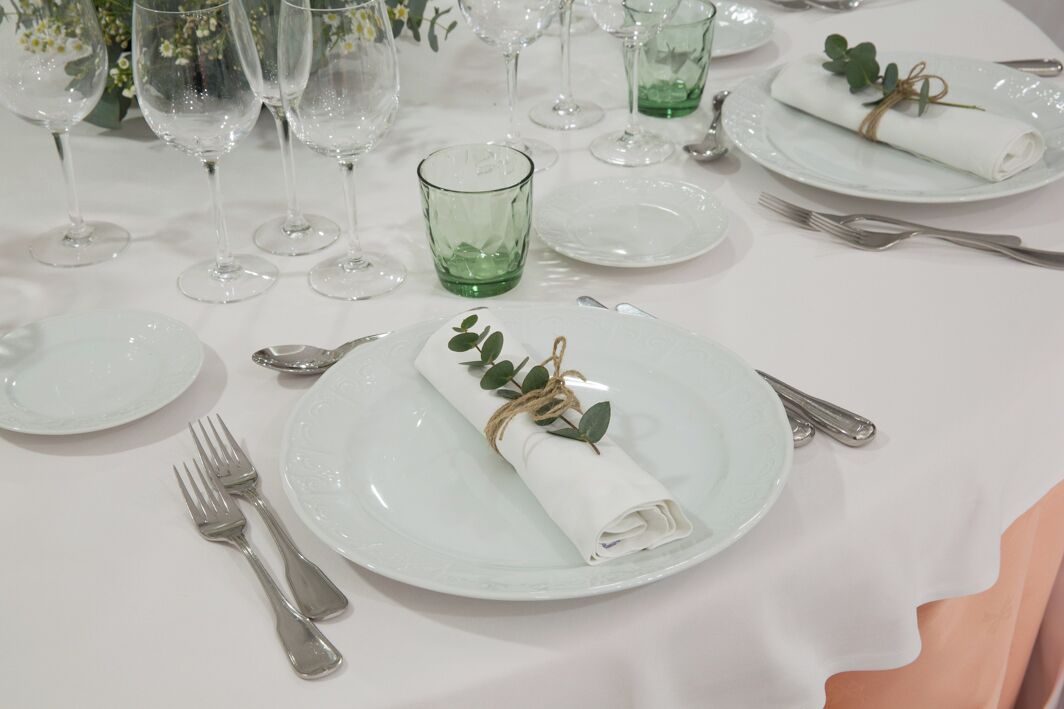 Une table dressée pour un dîner formel, avec de la vaisselle transparente, des couverts en argent et des serviettes pliées avec soin, maintenues par de la ficelle.
