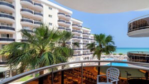 A balcony with a poolside view, palm trees, and a high-rise hotel building in the background. - Hotel & Spa Peñíscola Plaza Suites (Peniscola)