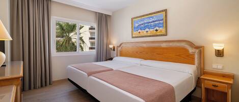 Habitación de hotel con una cama grande, una mesita de noche, una lámpara, un cuadro y una ventana con cortinas.