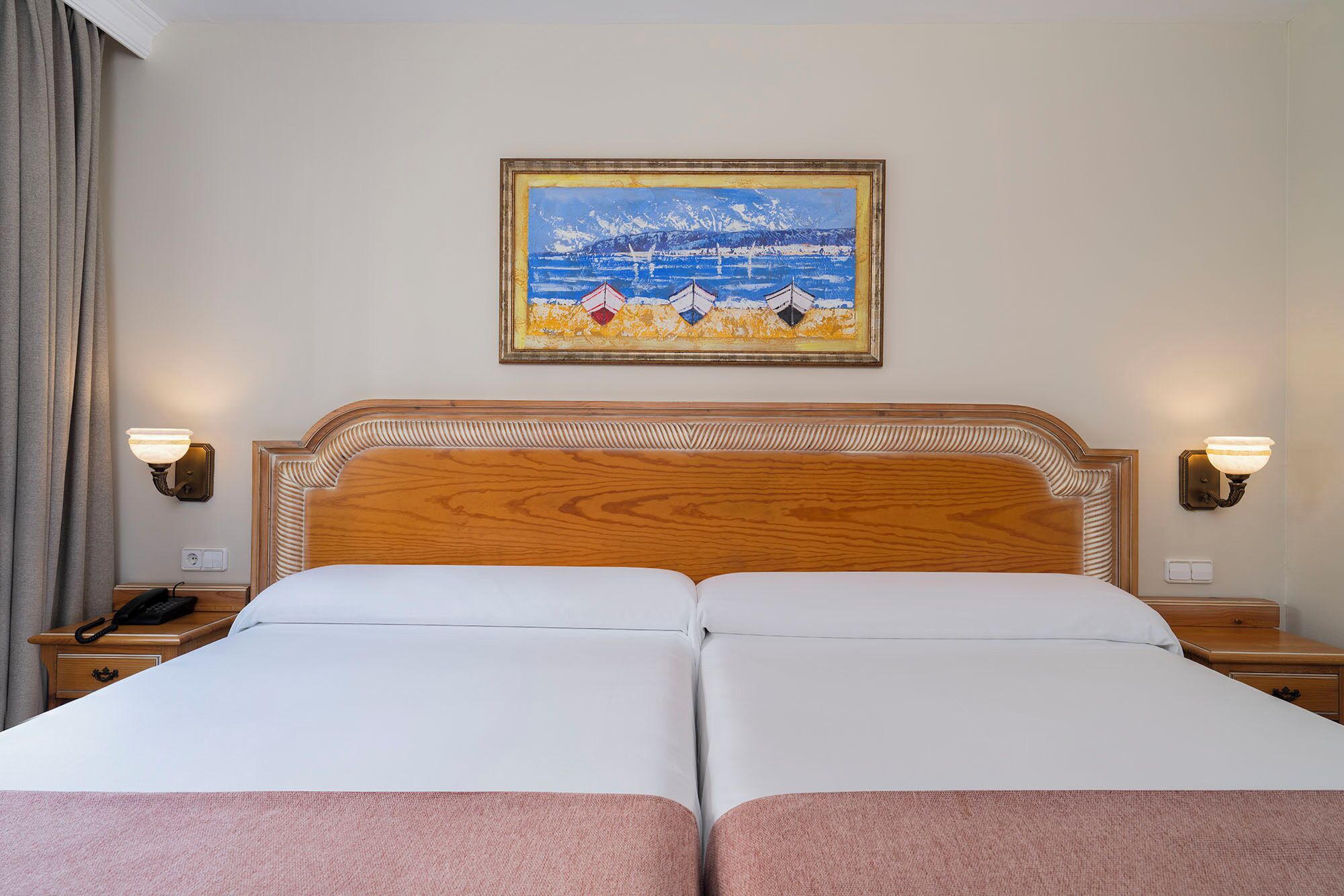 Habitación de hotel con una cama doble, dos mesitas de noche, una lámpara a cada lado y un cuadro enmarcado en la pared.