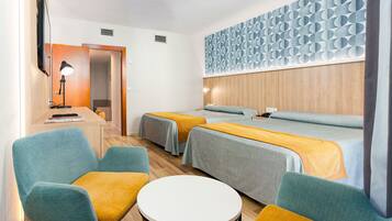 A hotel room with two beds, a desk with a lamp, a small round table, and a wall with a geometric pattern.