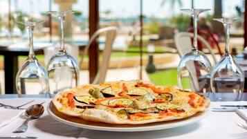 Pizza con diferentes verduras sobre un plato, colocada sobre una mesa con copas de vino y cubiertos.
