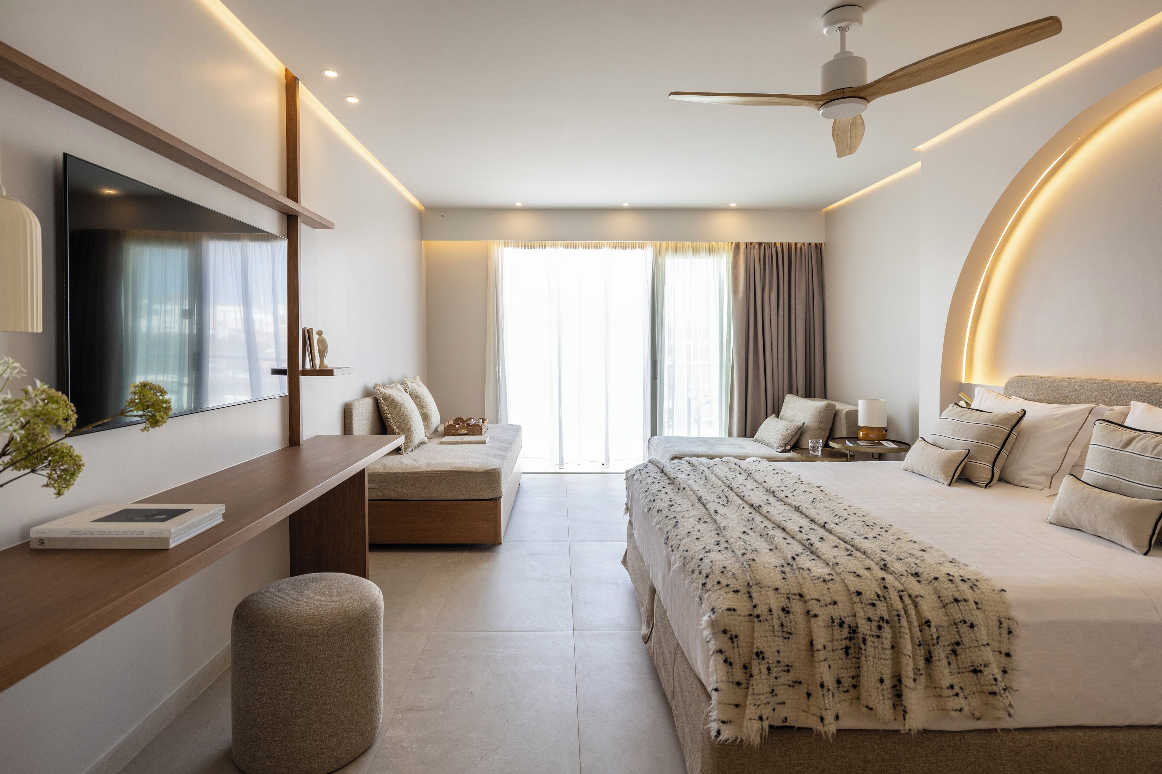 A modern hotel room with a bed, bedside table, TV, and a ceiling fan.