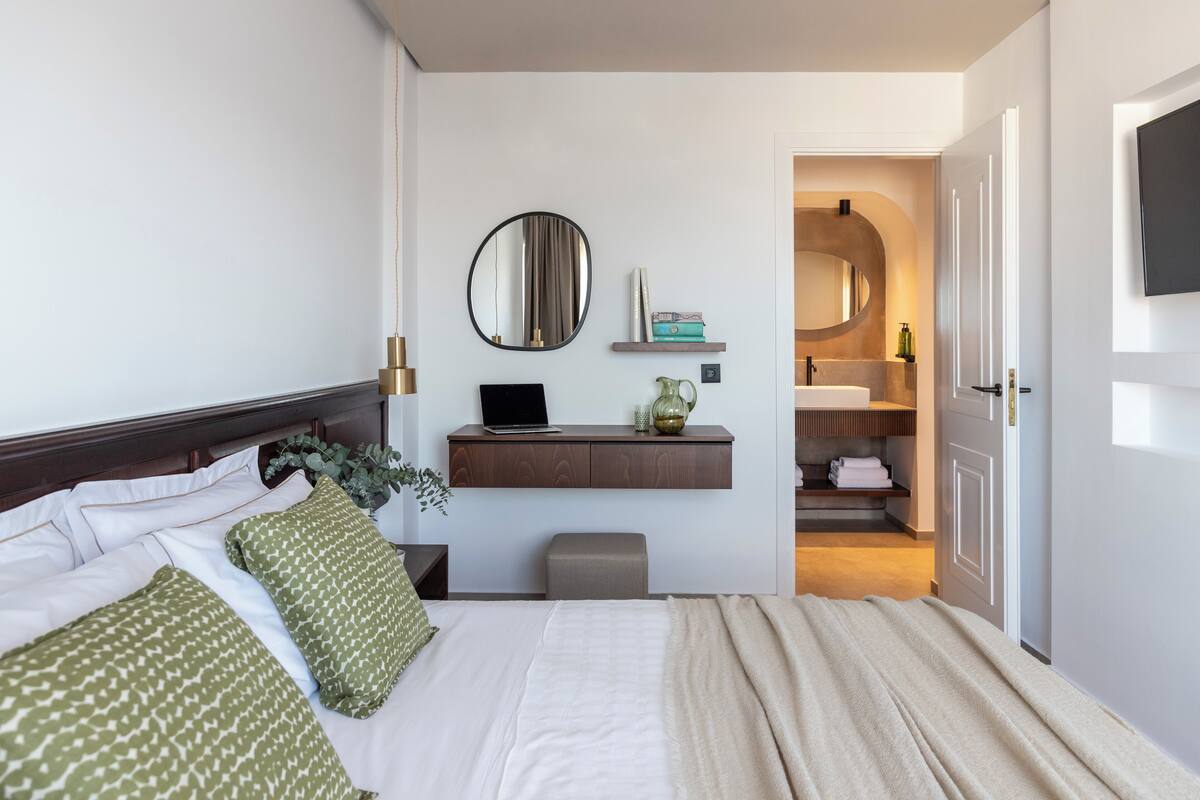 A hotel room with a bed, bedside table, lamp, and a view into the bathroom.