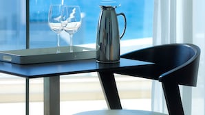 A table with two wine glasses and a coffee pot, a chair, and a view of the ocean through a window with the text "ALBATROS" on it. - Albatros Spa & Resort Hotel (Hersonissos)