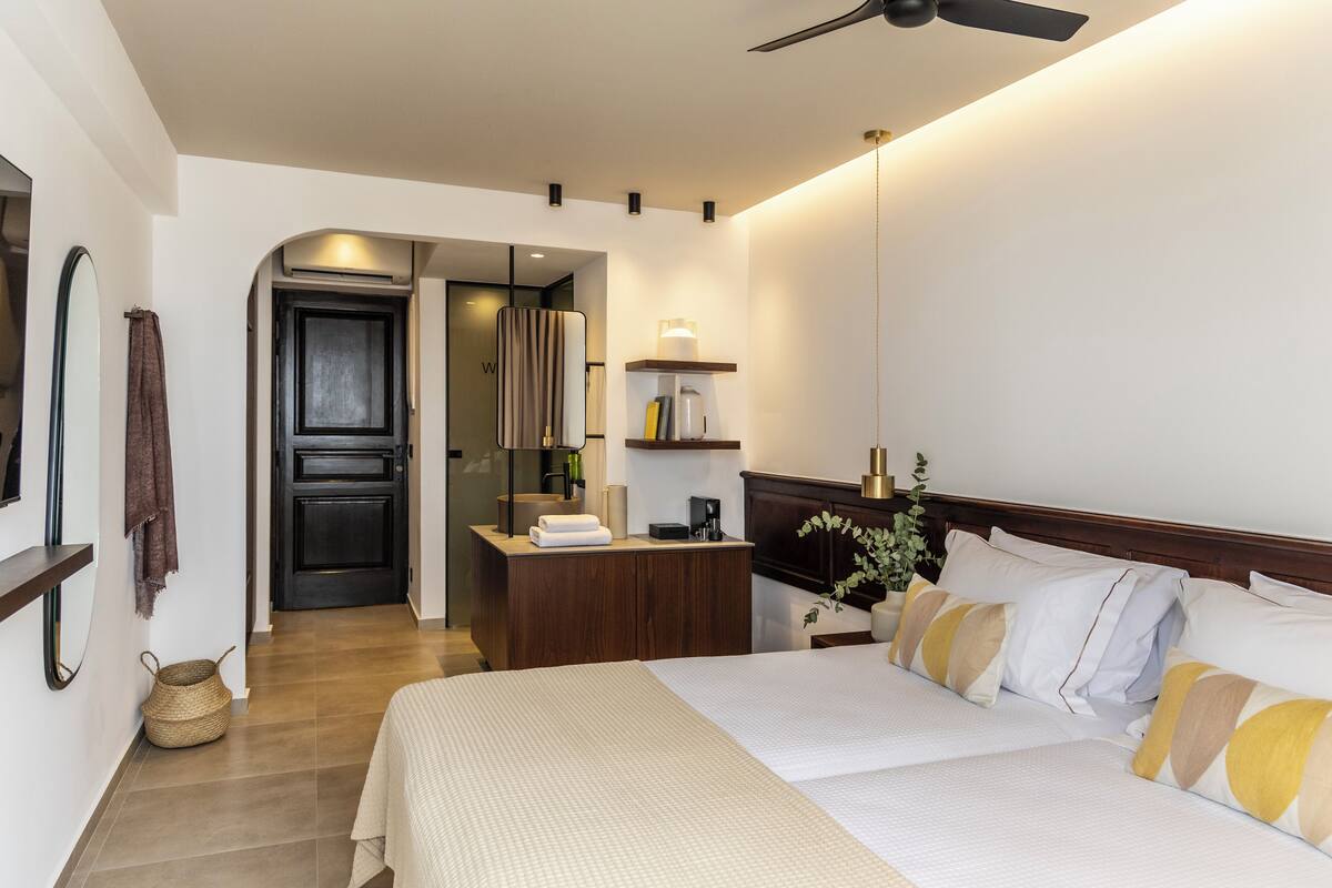 A modern hotel room with a large bed, a bedside table, a desk, and a ceiling fan.