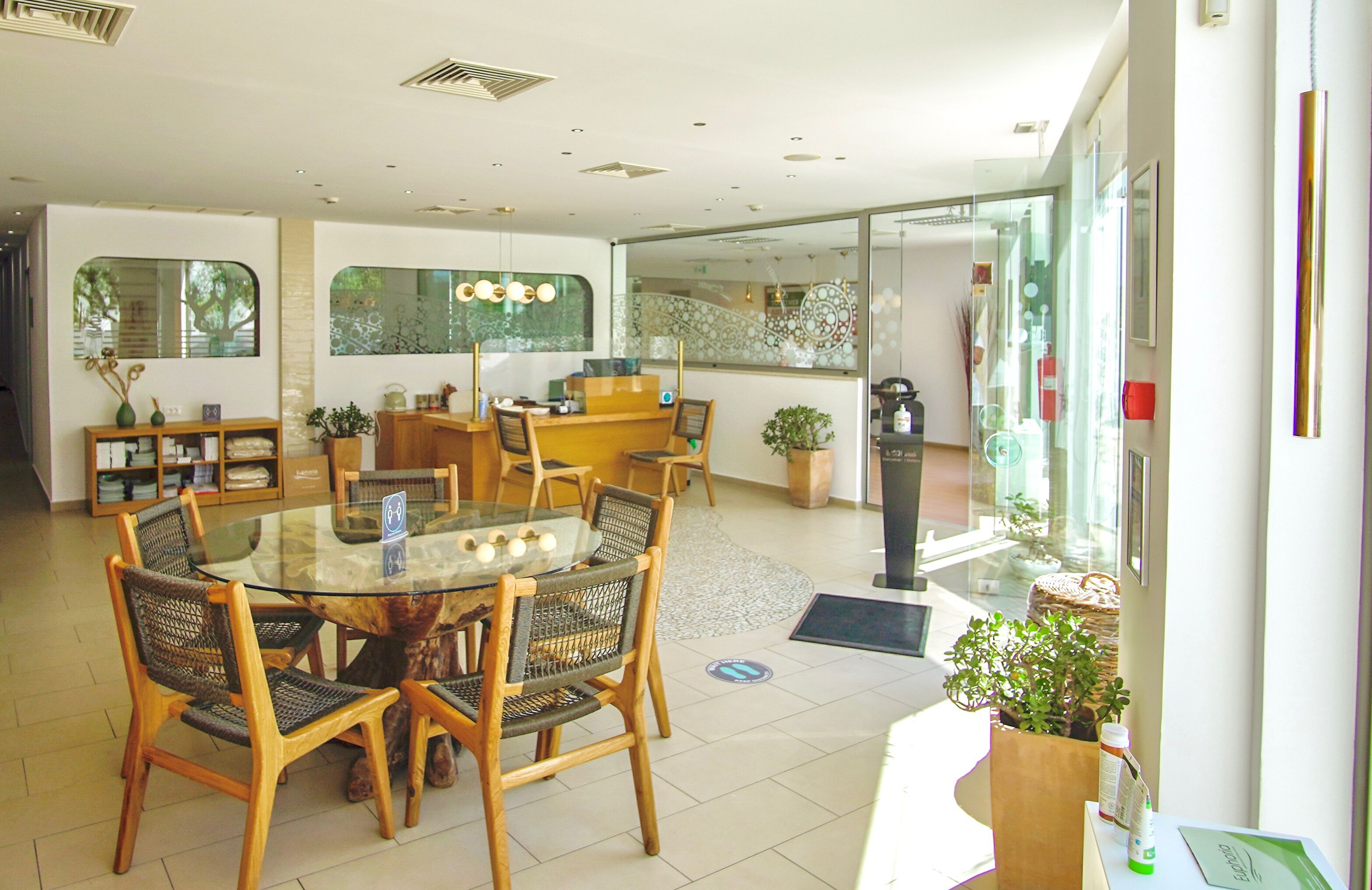 Una hall d'albergo moderna con un tavolo rotondo in vetro, sedie di legno, una reception e vista panoramica attraverso una parete di vetro.