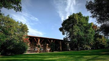 A rustic building with a stone facade and wooden beams, surrounded by lush greenery and a well-maintained lawn.