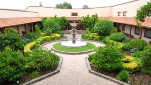 Un patio central con una fuente, rodeado de jardines bien cuidados y un edificio con tejado de azulejos.