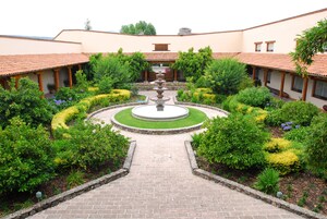 A courtyard with a central fountain, surrounded by well-maintained gardens and a building with a tiled roof.