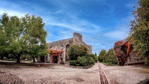 Un edificio histórico de piedra con una entrada arqueada, rodeado de árboles y un camino adoquinado.