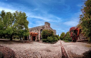 A historic stone building with an arched entrance, surrounded by trees and a cobblestone pathway.