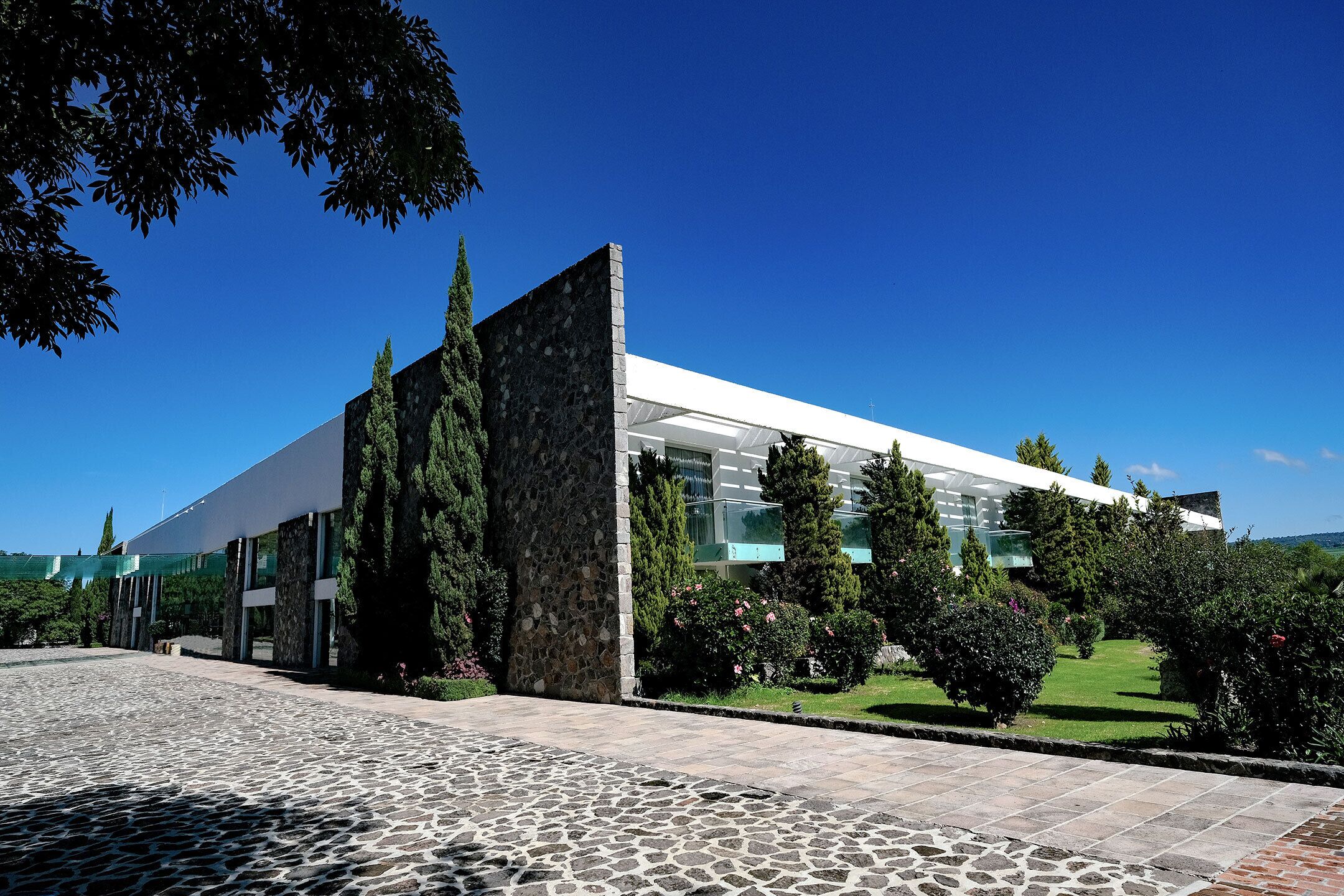 A modern building with a stone facade, large windows, and a well-maintained garden.