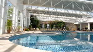 Una piscina interior con suelo de baldosas, rodeada de sillones y plantas en macetas.