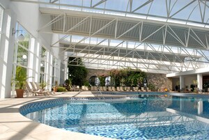 Uma piscina interior com chão revestido, rodeada por espreguiçadeiras e plantas em vasos.