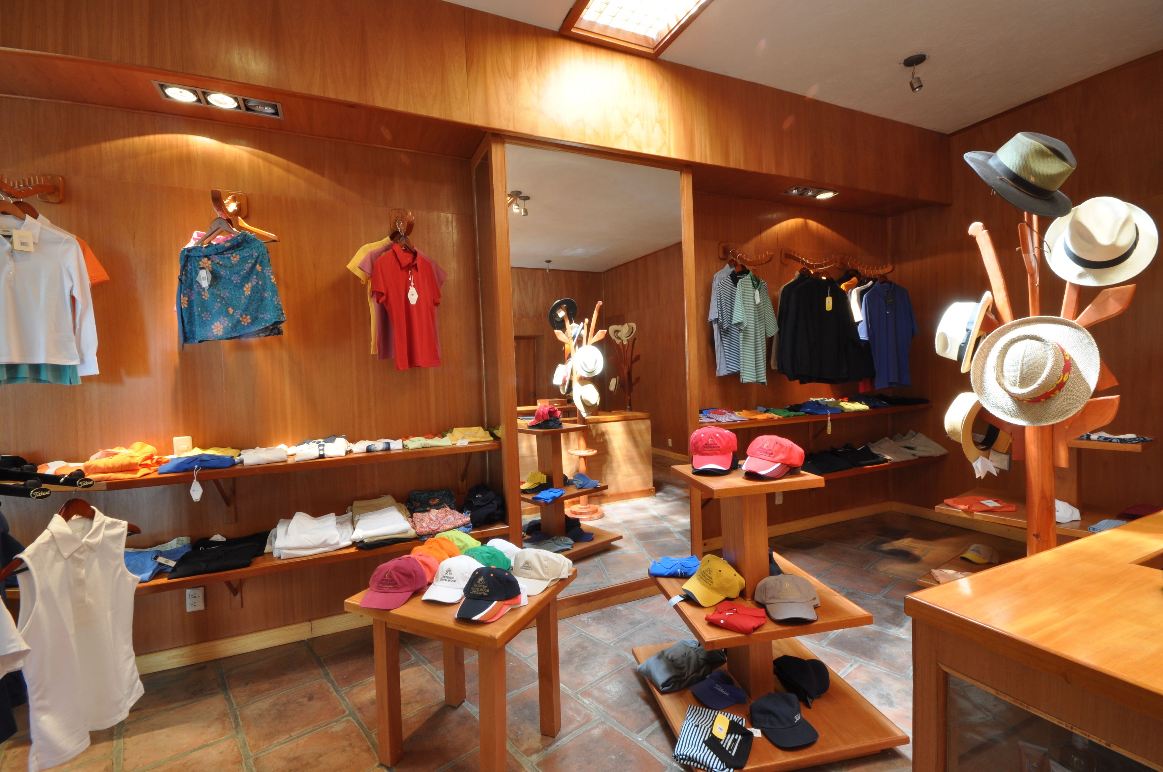 A clothing store with racks of shirts and hats, wooden shelves, and a mirror.