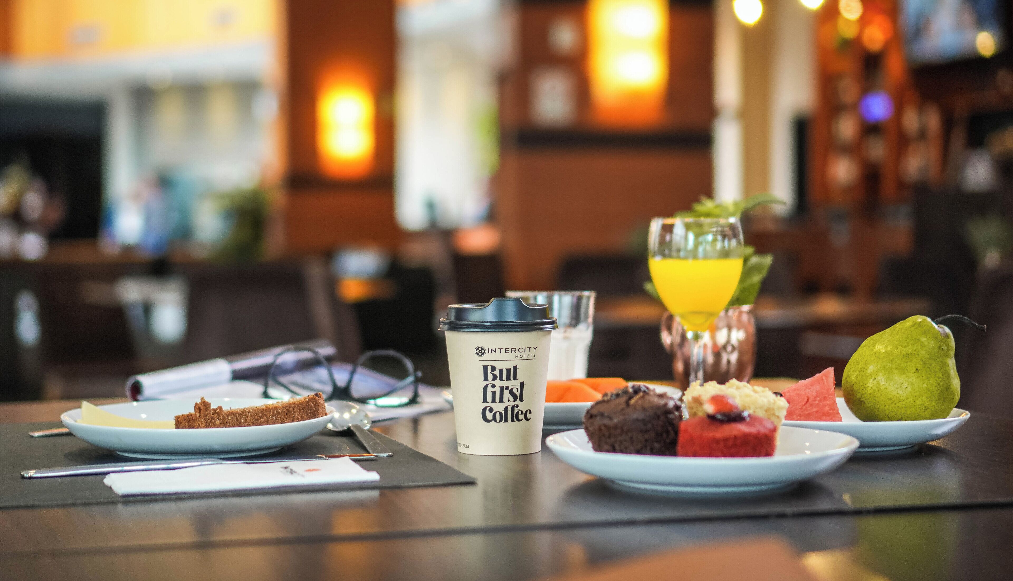 Une table dressée pour le petit-déjeuner, avec une tasse de café, un verre de jus d’orange et diverses pâtisseries.