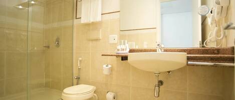Un baño moderno con cabina de ducha de vidrio, inodoro, lavabo y secador de pelo fijado a la pared.