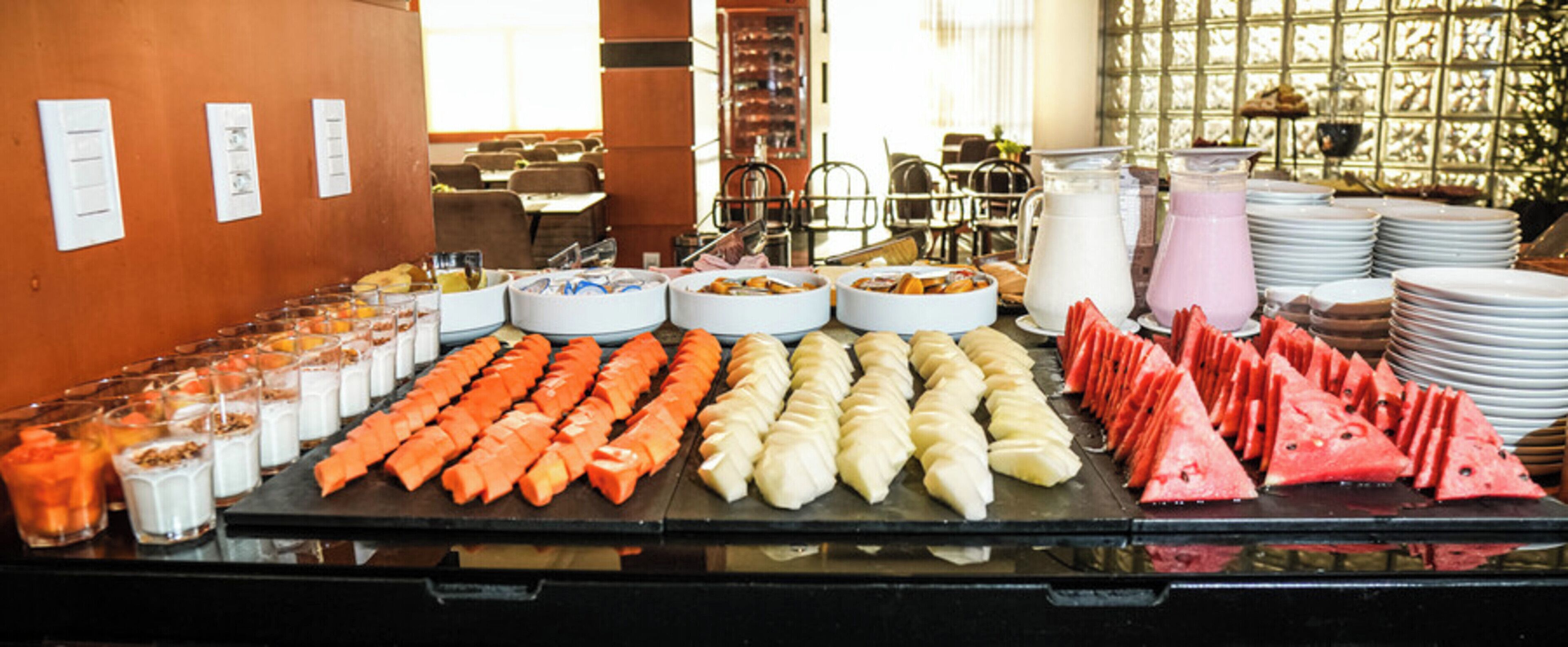 Buffet com diversos alimentos, incluindo frutas fatiadas, legumes e produtos lácteos.
