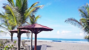 A beach with palm trees, lounge chairs, and a red umbrella. - Las Olas Resort (Guarumal)