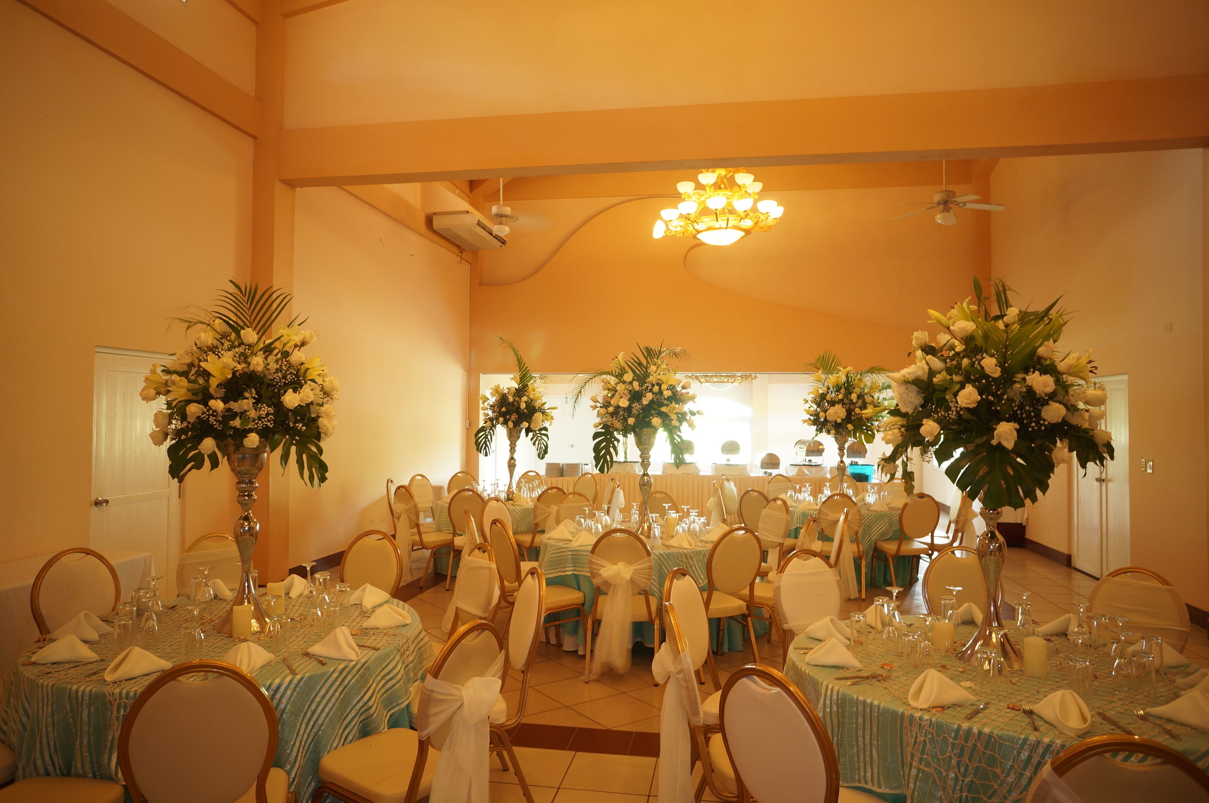 A banquet hall with round tables, chairs, and floral centerpieces.