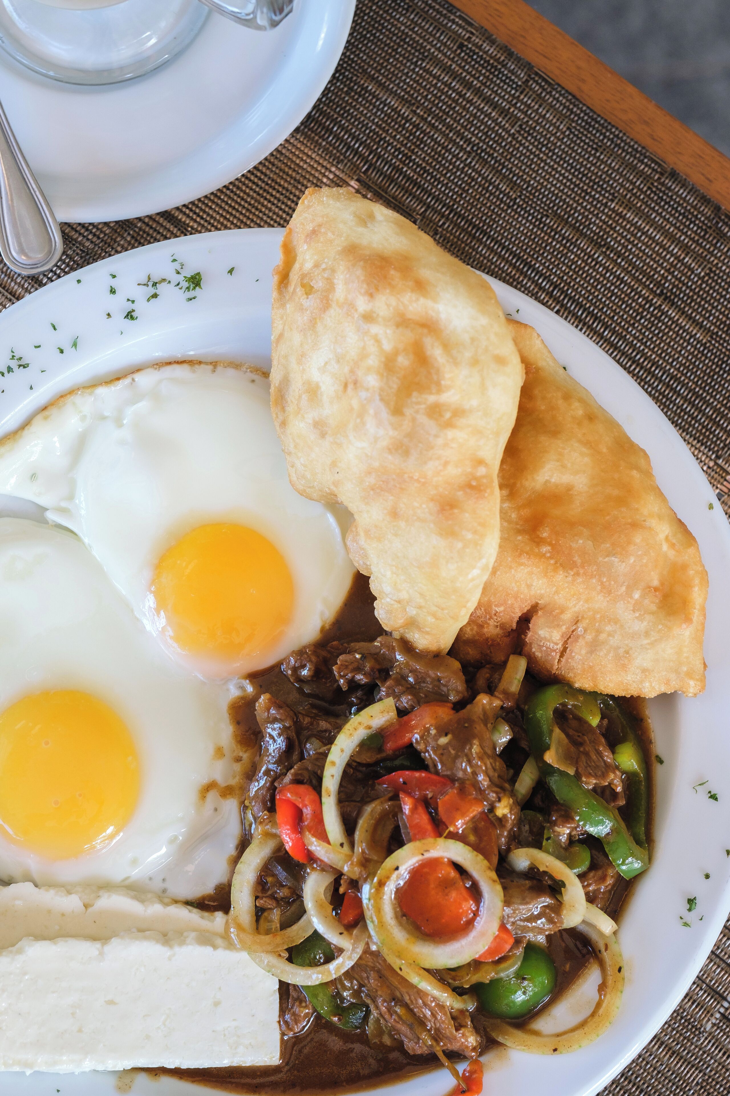 A plate with two sunny-side-up eggs, a piece of fried bread, and a beef stir-fry with vegetables.