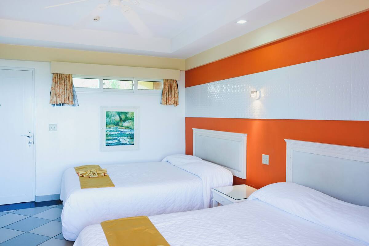 A hotel room with two beds, a white door, and a painting on the wall.