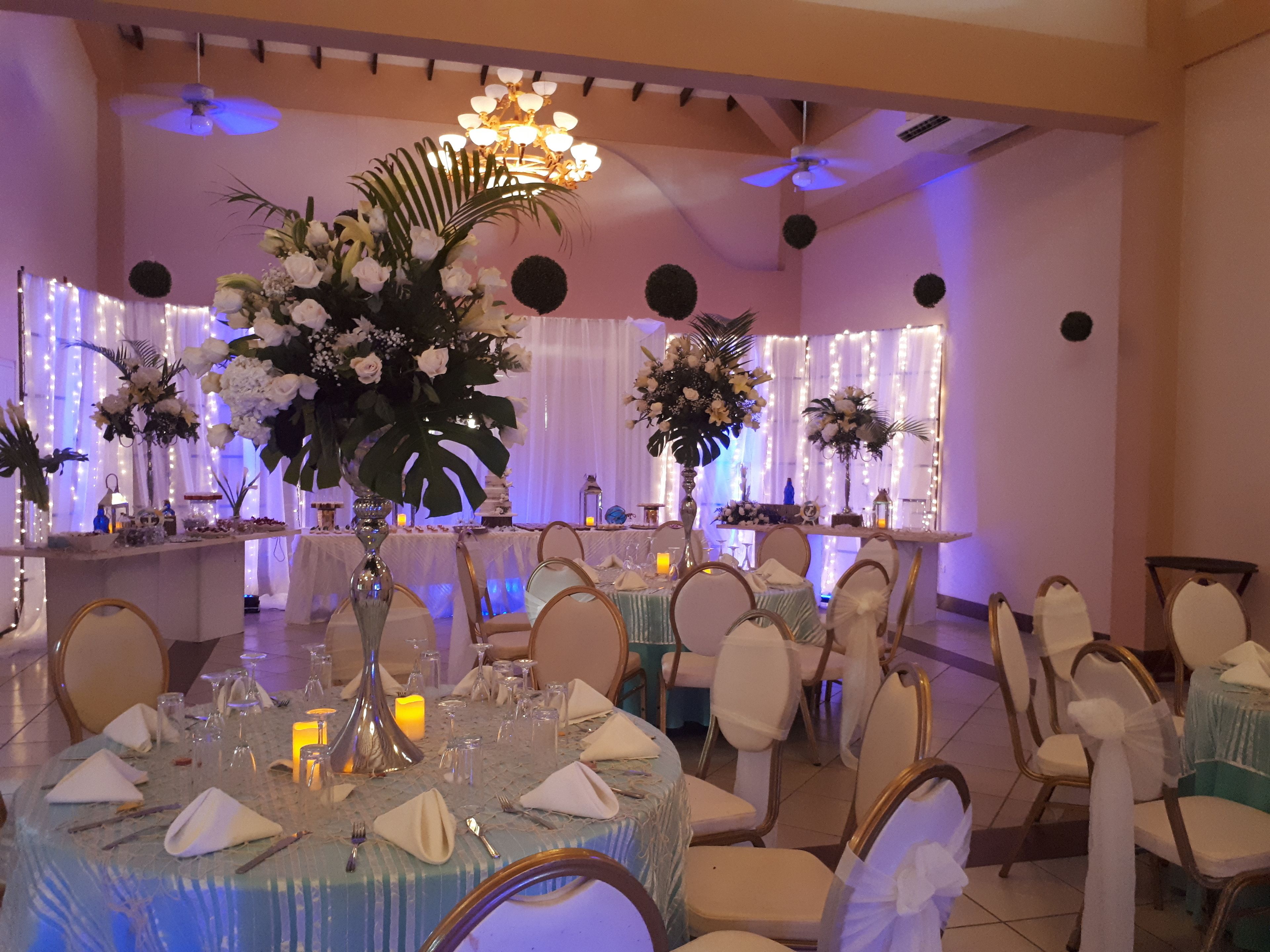 A banquet hall with round tables set for a formal event, featuring floral centerpieces and table settings.