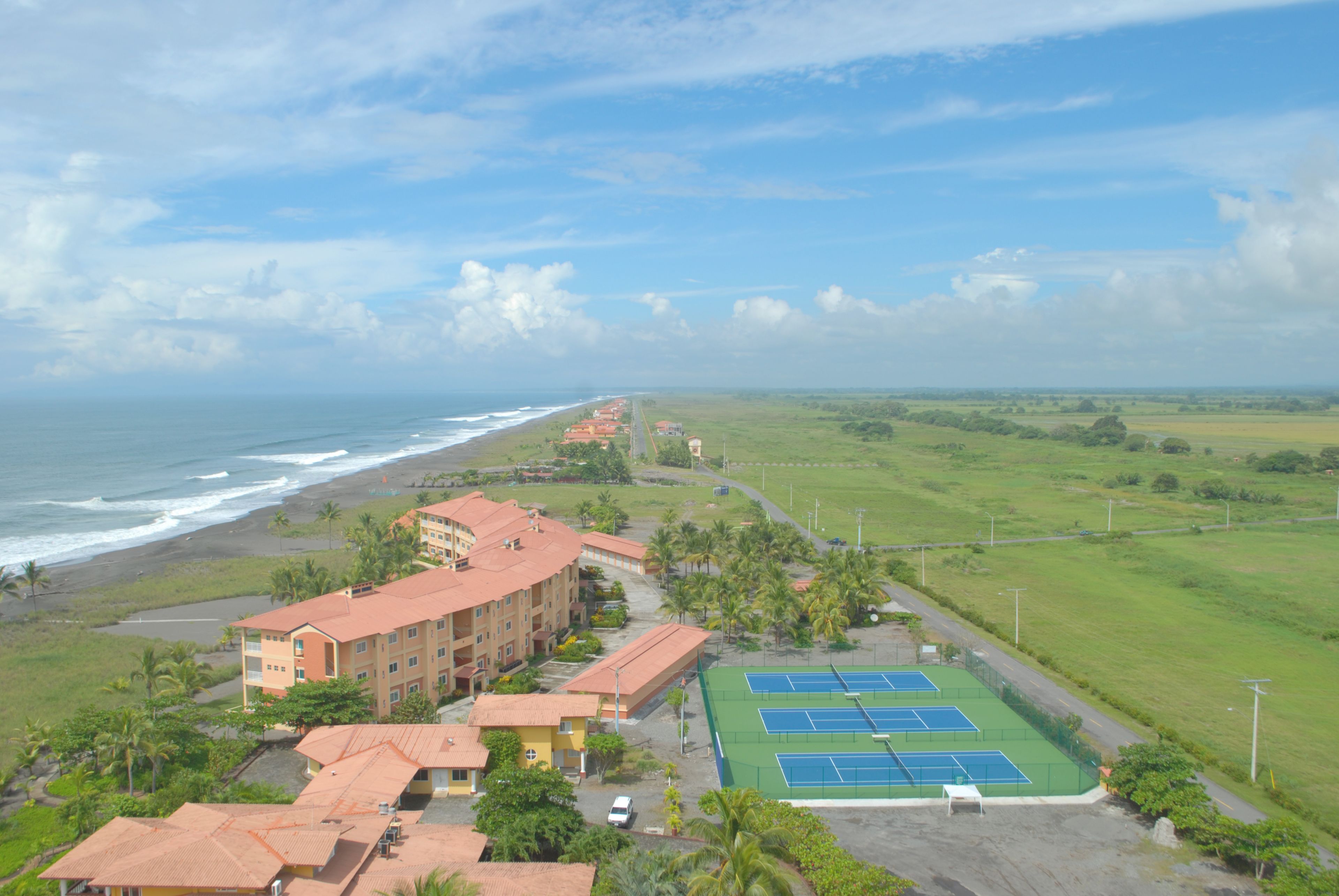 A coastal hotel with a tennis court, beachfront view, and multiple buildings.