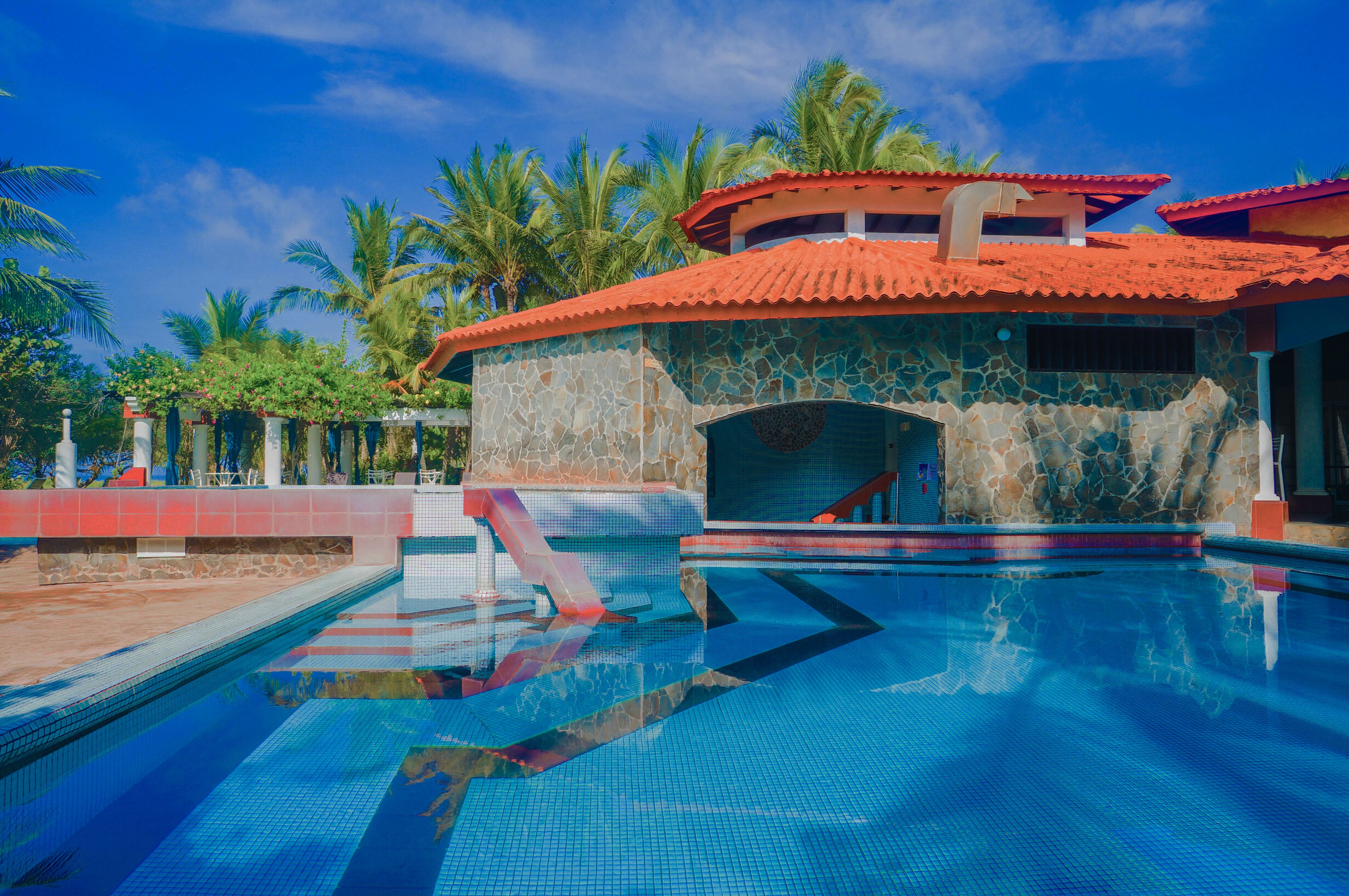 A swimming pool with a stone wall and a red-roofed structure.