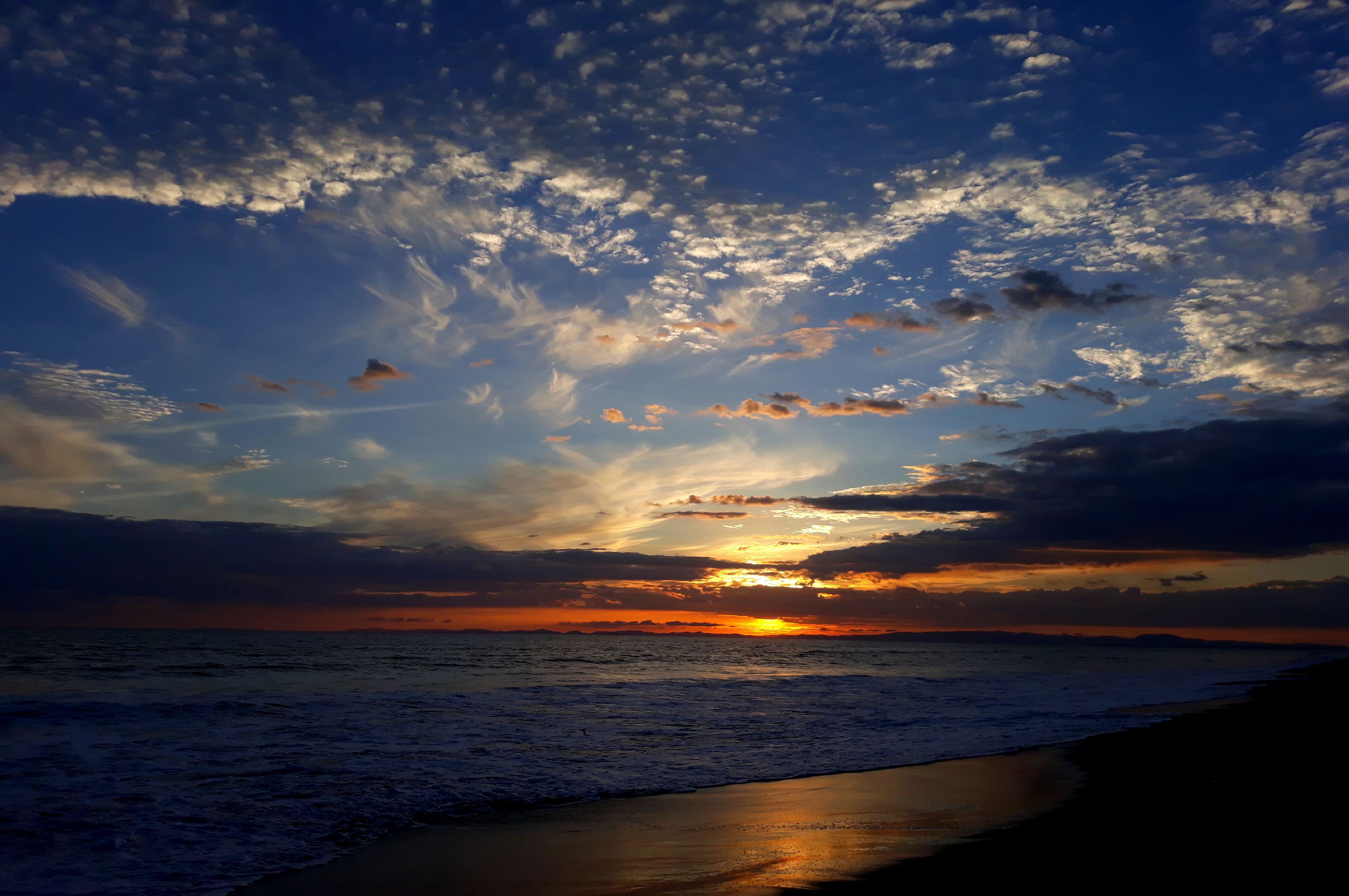 A sunset over the ocean with a beach in the foreground.