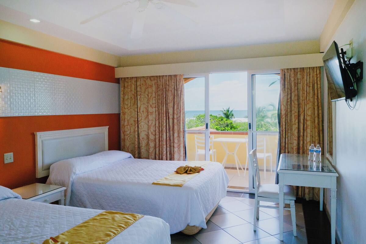 A hotel room with two beds, a desk, and a view of the ocean.