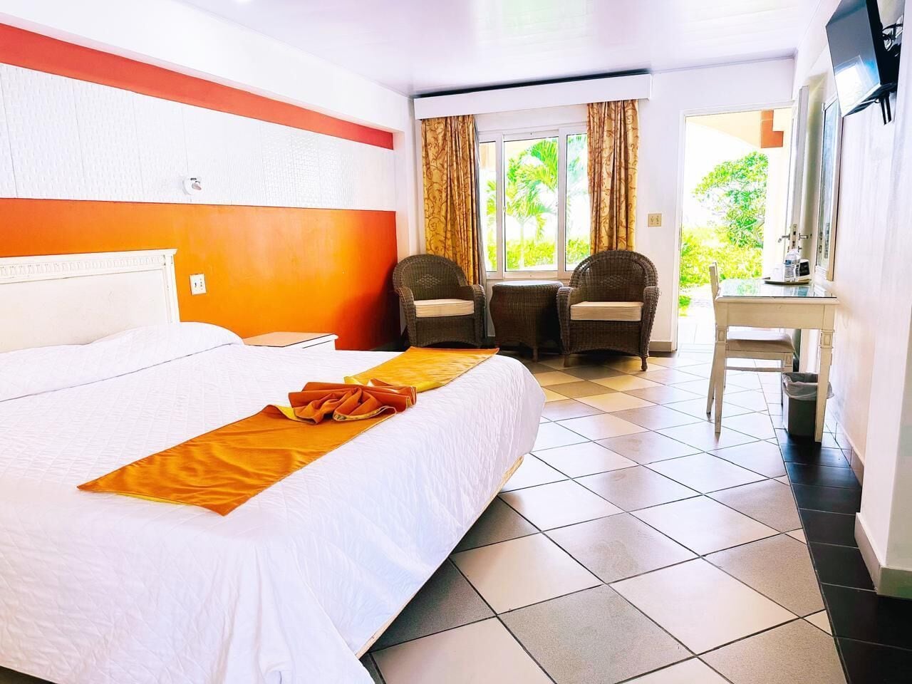 A hotel room with a large bed, two chairs, a small table, and a TV.
