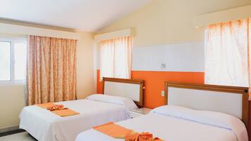 Quarto de hotel com duas camas de solteiro, cada uma com uma toalha laranja e roupa de cama branca. O quarto tem paredes laranja e uma janela com cortinas estampadas.