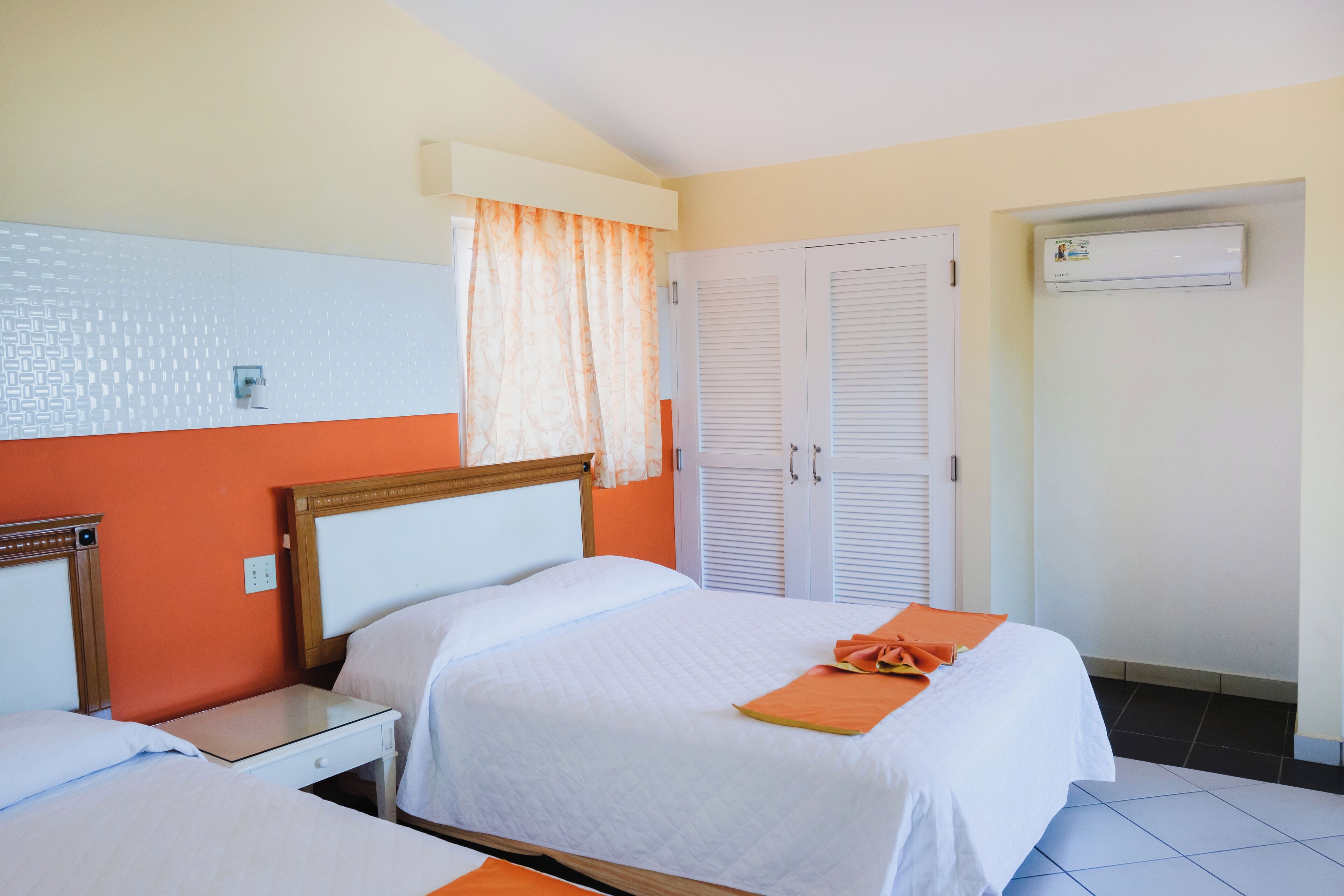 A hotel room with a bed, a nightstand, a wardrobe, and an air conditioning unit.