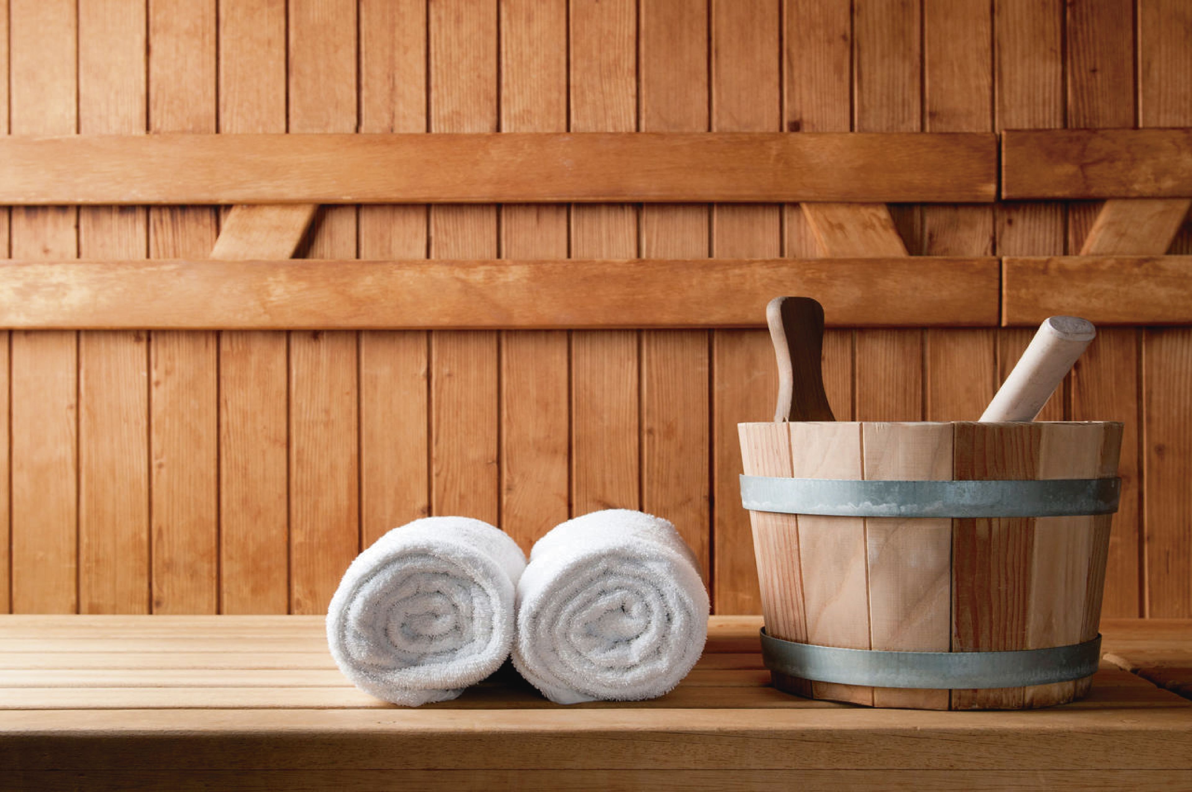A wooden bench with two rolled white towels and a wooden bucket with a metal band and a wooden mallet.