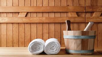 A wooden bench with two rolled white towels and a wooden bucket with a metal band and a wooden mallet.