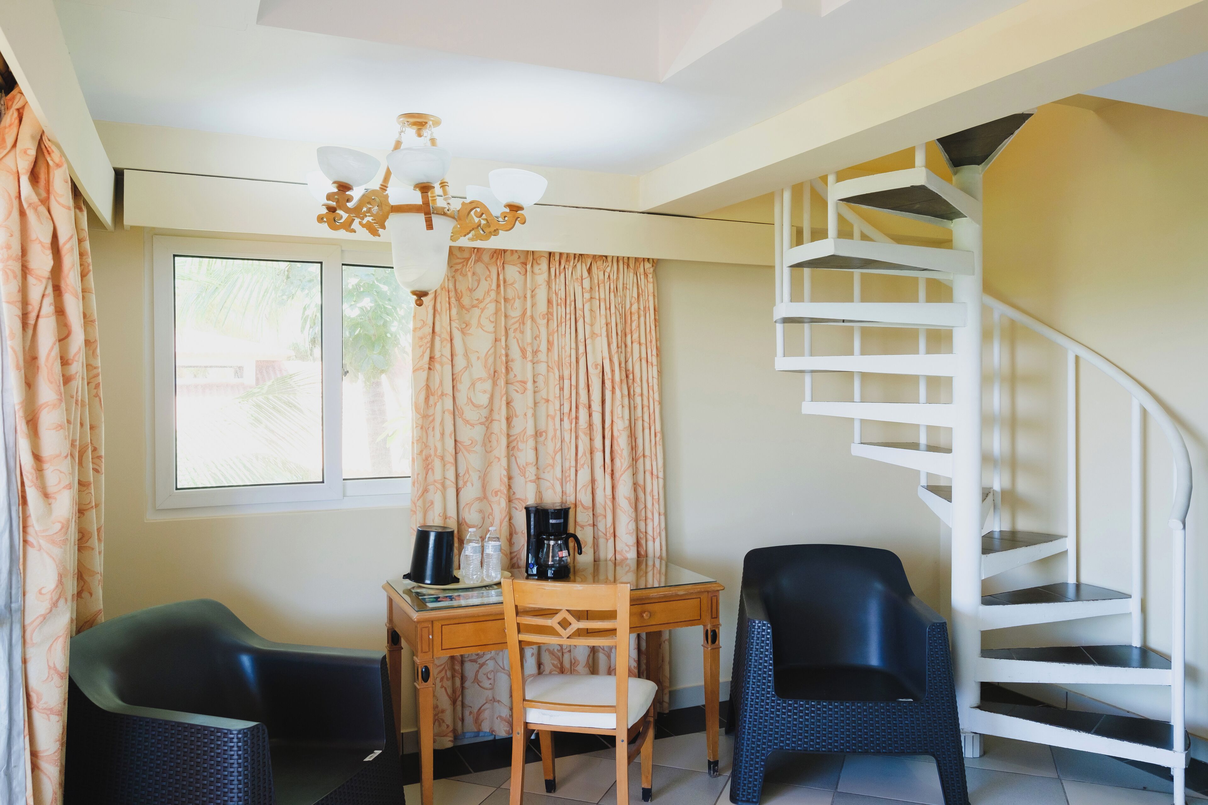 A room with a spiral staircase, a wooden desk with a chair, a black chair, and a window with curtains.